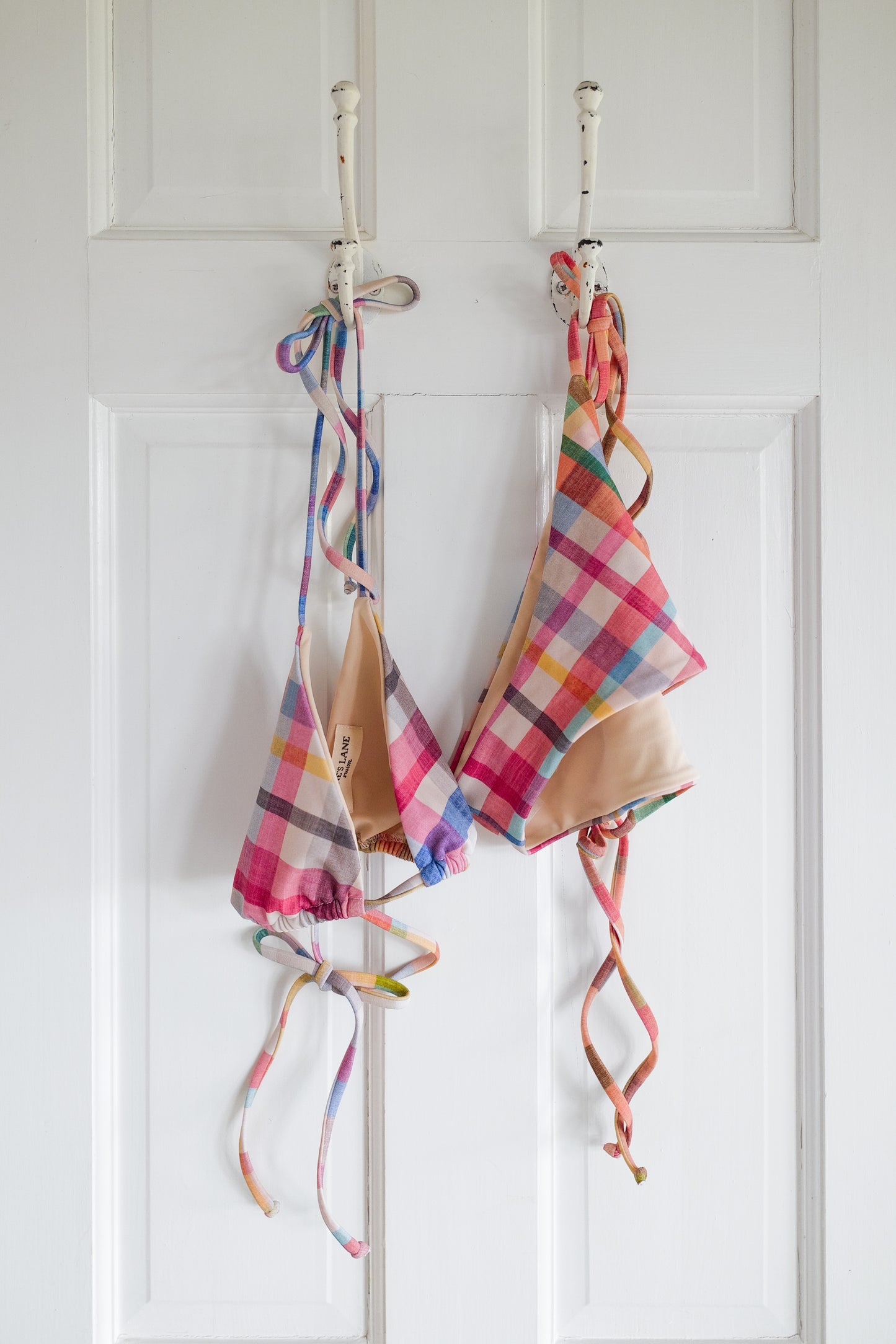 Plaid string bikini hanging on a rack against a white wall.