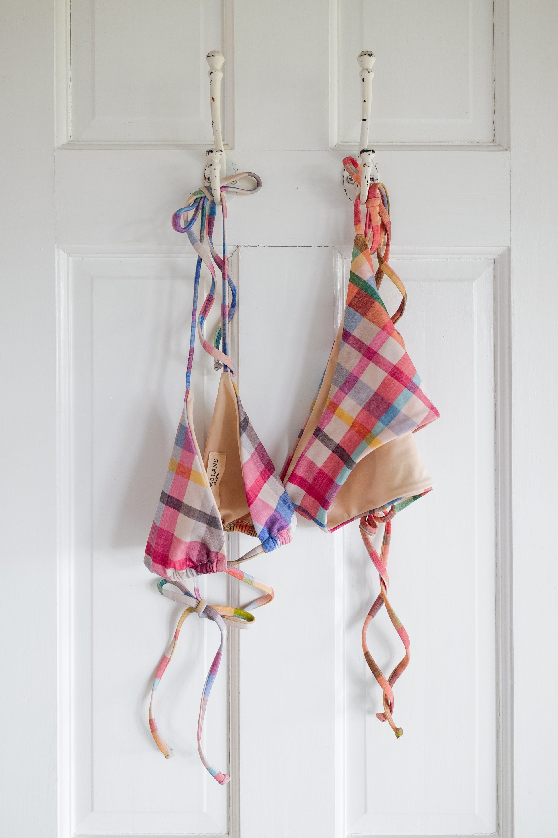 Plaid string bikini hanging on a rack against a white wall.