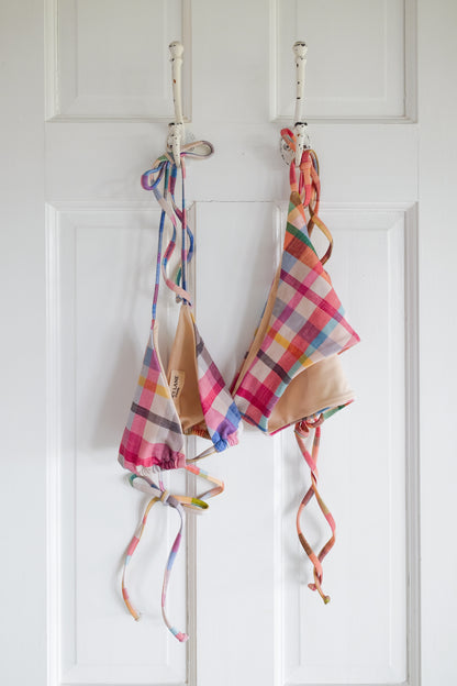Plaid string bikini hanging on a rack against a white wall.