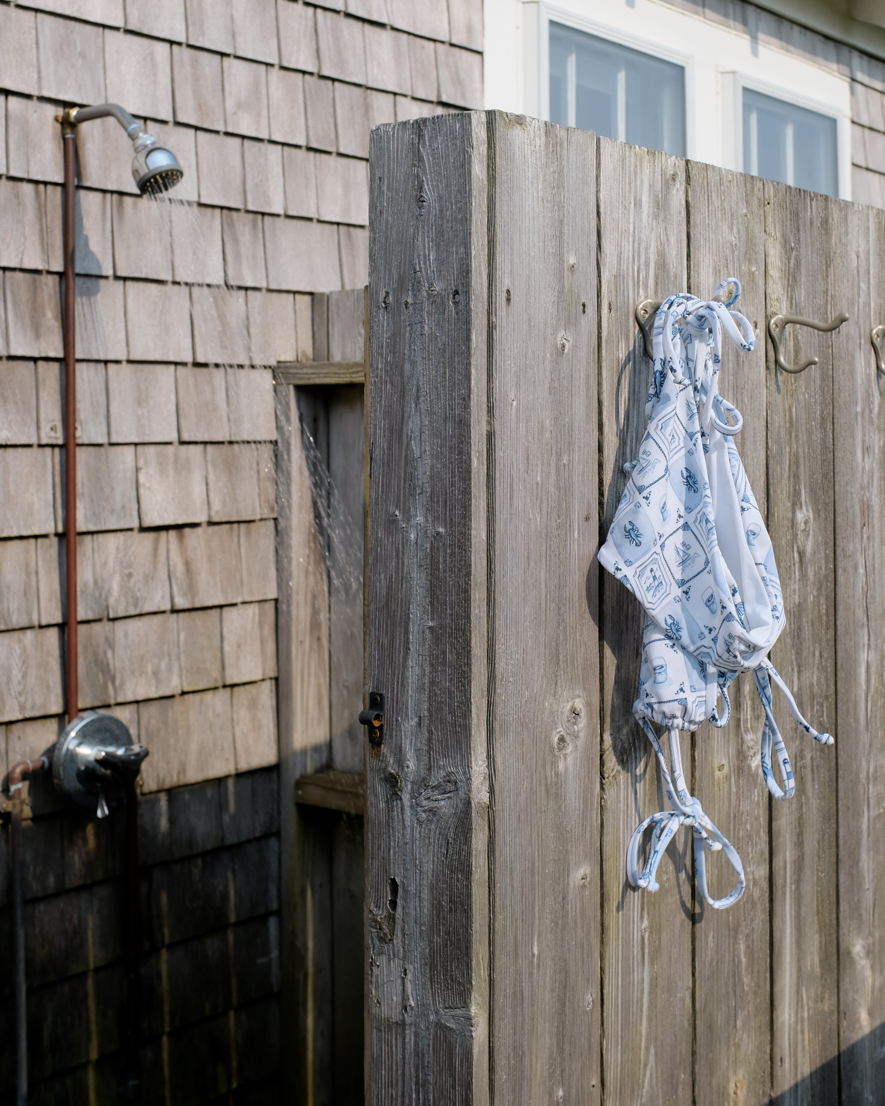 Outdoor shower with wooden wall and hanging swimsuit.