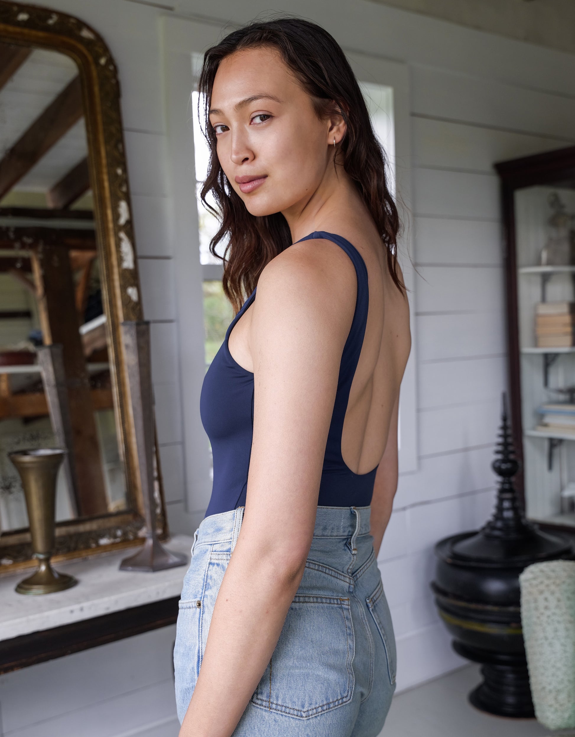 Woman wearing a navy blue tank top with cut-out design in a room with white walls and decorative items.